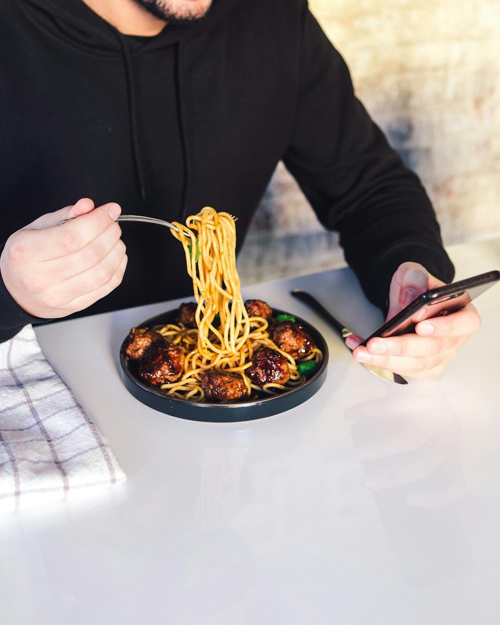 A guest eating noodles while ordering on a phone
